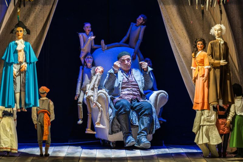 foto di scena. Sior Todero brontolon seduto su una poltrona, circondato da marionette