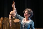 Foto di scena. Donna tiene in mano il torso senza testa né gambe di una bambola