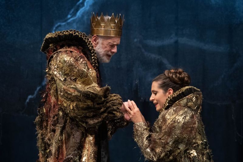 Foto di scena. Una donna tiene le mani di Re Lear