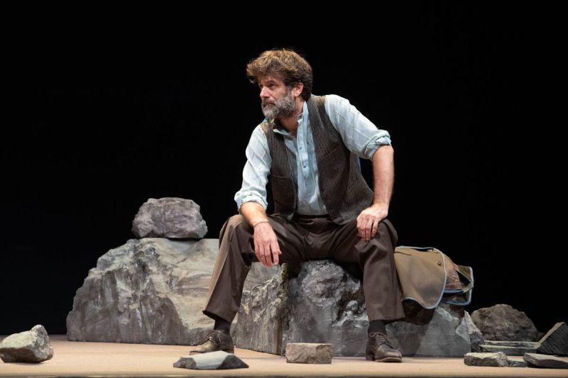 Foto di scena. Uomo seduto su un masso su sfondo nero 