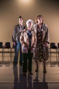 Foto di scena. Ariella Reggio, Maria Ariis e Lucia Limonta in piedi, vicine, guardano verso il pubblico